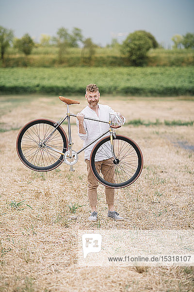 Man with handcrafted racing cycle on stubble field