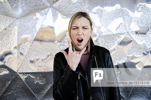 Porträt einer schreienden jungen Frau  die ein Rock-and-Roll-Zeichen zeigt