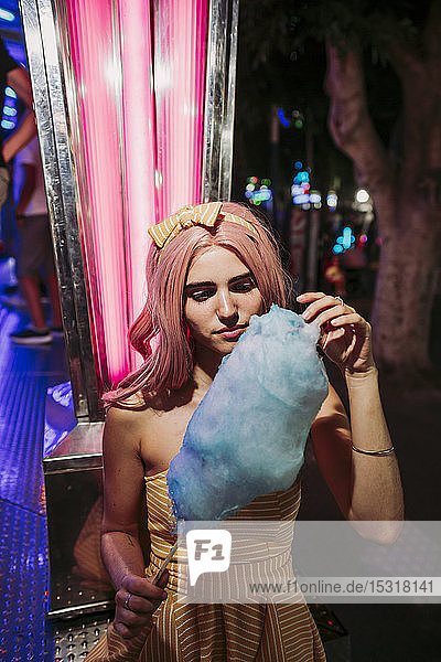 Portrait of a young woman with cotton candy on a funfair at night