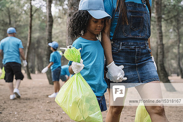 Frau und Mädchen gehen Hand in Hand und sammeln Müll in einem Park