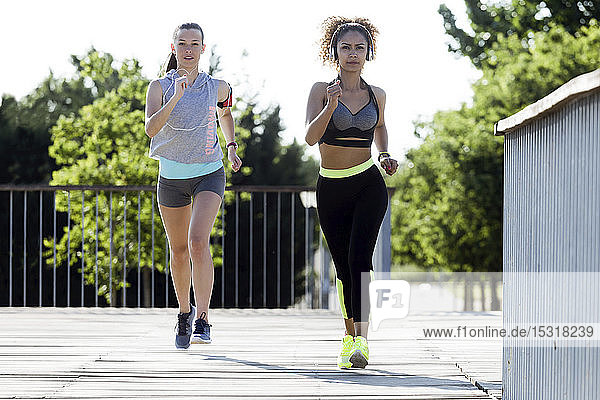 Two sporty young women running on a bridge