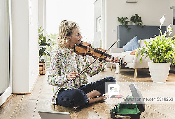 Frau mit Tablette sitzt zu Hause auf dem Boden und spielt Geige