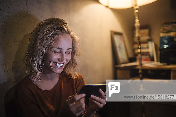 Portrait of laughing young woman using smartphone at home
