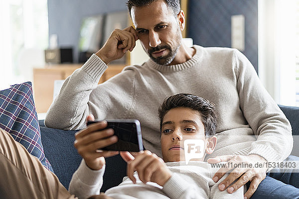 Father and son using smartphone on couch in living room