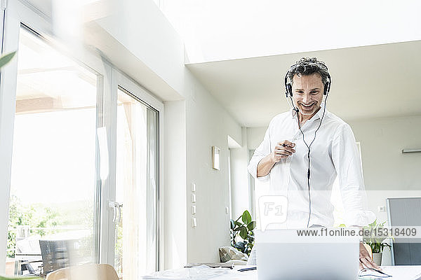 Businessman in bright office having conference call using headset and laptop