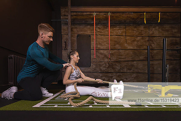 Junge Frau trainiert im Fitness-Studio mit einem persönlichen Trainer  der am Seil zieht