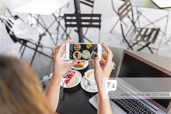 Junge Bloggerin sitzt im Straßencafé und fotografiert Essen  Teilansicht