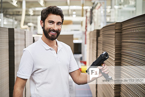 Porträt eines lächelnden Mannes in einer Fabrikhalle mit Barcode-Scanner