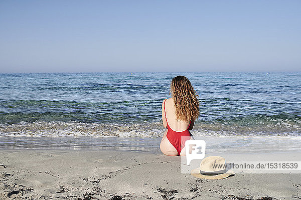Rückansicht einer am Strand sitzenden jungen Frau