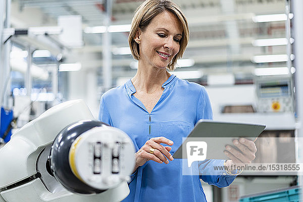 Geschäftsfrau mit Tablette am Montageroboter in einer Fabrik