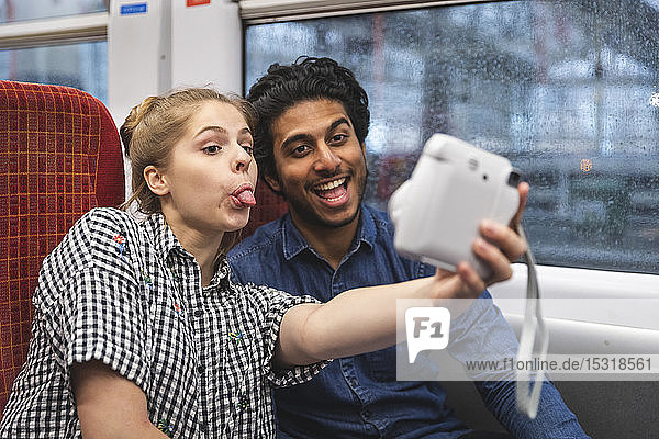 Porträt von Freunden  die sich beim Selbstporträt mit Sofortbildkamera im Zug amüsieren  London  UK