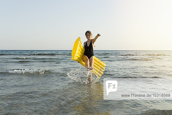 Junge Frau mit gelbem Luftbett am Strand
