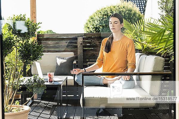 Junge Frau  die auf einer Couch auf der Terrasse sitzt und Yoga praktiziert