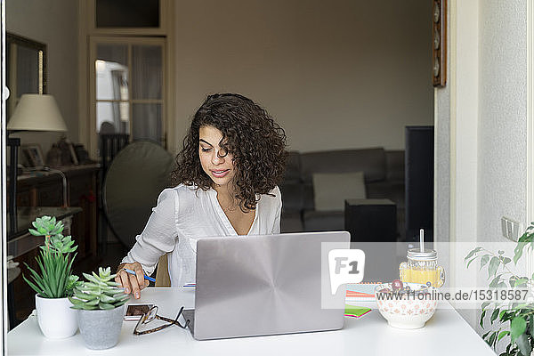 Young woman using cell phone and laptop at desk