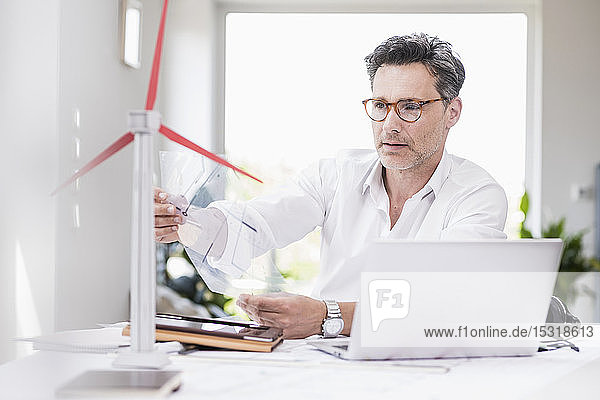 Businessma n sitting in office using laptop looking at model of a windwheel