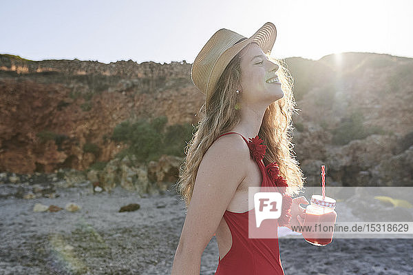 Happy young woman with a smoothie walking on the beach