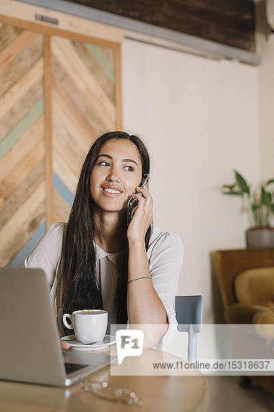 Junge Geschäftsfrau mit Laptop telefoniert am Tisch in einem Cafe