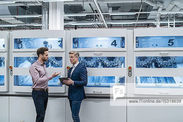 Two businessmen with tablet talking at machine in a modern factory