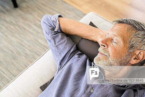 Senior man lying on couch at home taking a nap