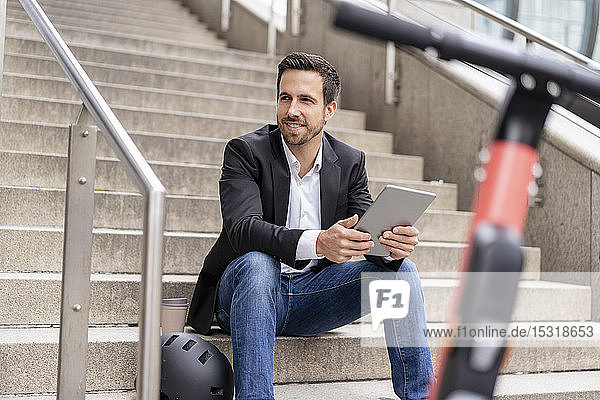 Businessman with e-scooter using tablet in the city