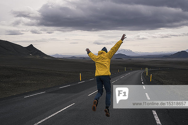 Glücklicher Mann springt vor Freude auf einer leeren Straße  Island