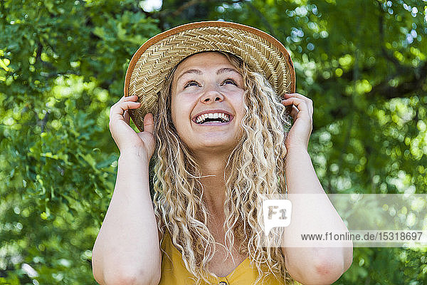 Porträt einer lächelnden blonden Frau mit Strohhut  Hände auf dem Hut