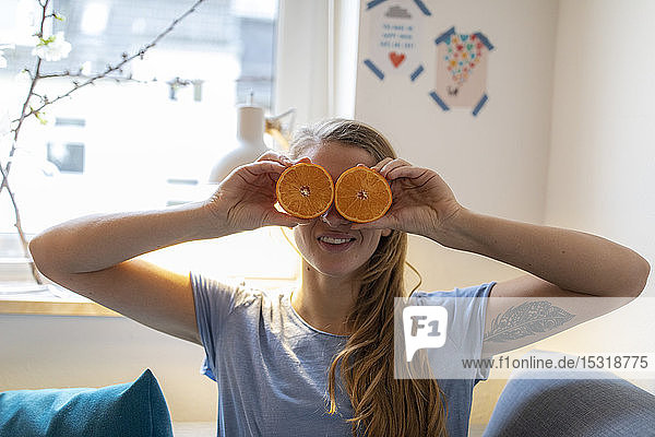 Playful young woman covering her eyes with oranges at home