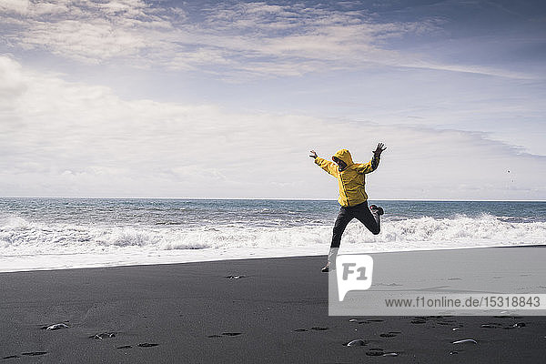 Reifer Mann springt vor Freude an einem Lavastrand in Island