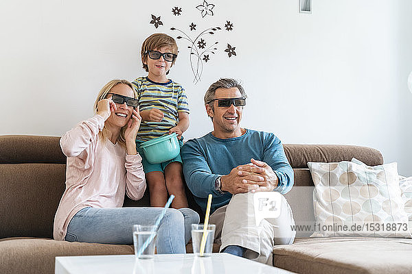 Vater  Mutter und Sohn tragen zu Hause auf der Couch eine 3D-Brille und sehen fern