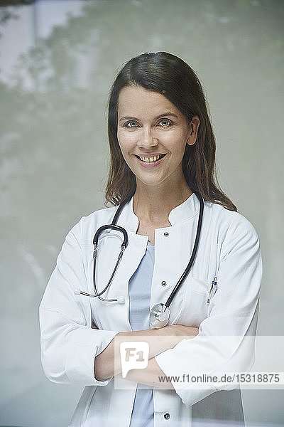 Porträt einer lächelnden Ärztin hinter einer Fensterscheibe