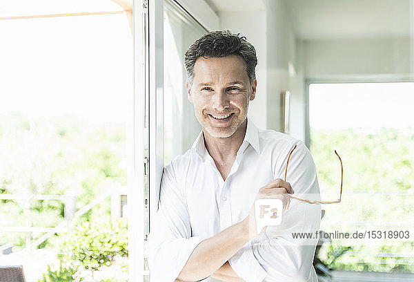 Mature man leaning on window holding his spectacles