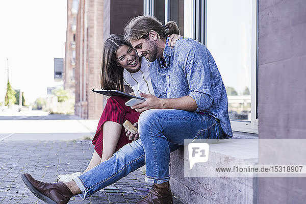 Junges Paar sitzt auf der Fensterbank eines Gebäudes und benutzt ein Tablett