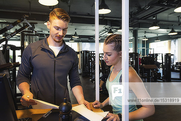 Young woman and personal trainer discussing plan in fitness gym