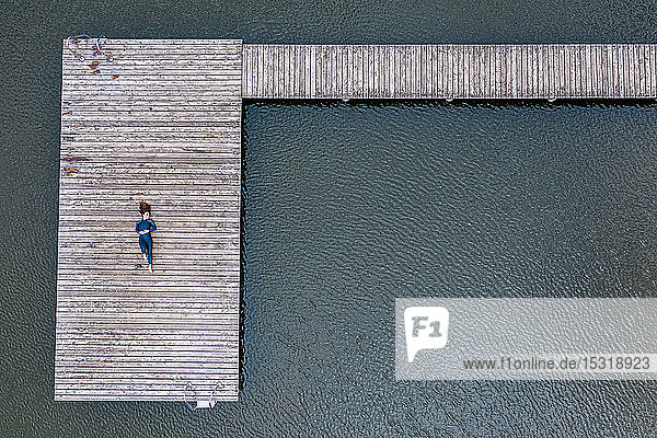 Luftaufnahme einer jungen Triathletin  die auf einem Steg an einem See liegt