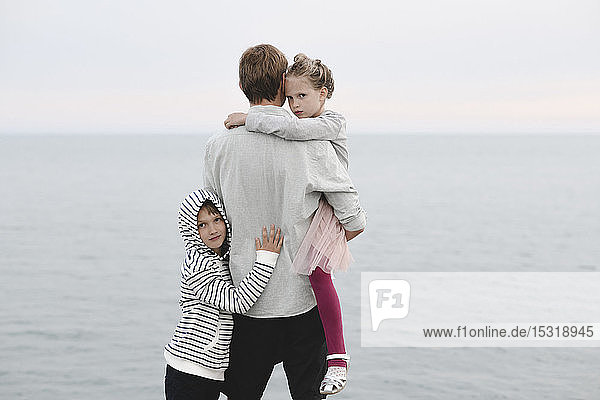 Rückenansicht eines am Meer stehenden Mannes mit kleiner Tochter und Sohn