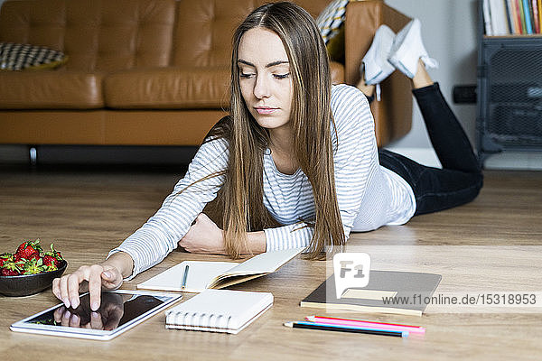 Junge Frau liegt zu Hause mit einer Tablette auf dem Boden