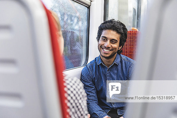 Porträt eines lächelnden jungen Mannes  der mit seiner Freundin im Zug reist  London  UK