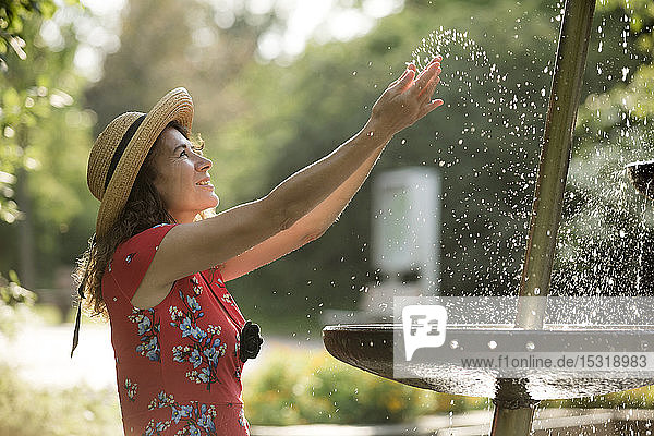Lächelnde Frau  die im Sommer mit Brunnenwasser spritzt