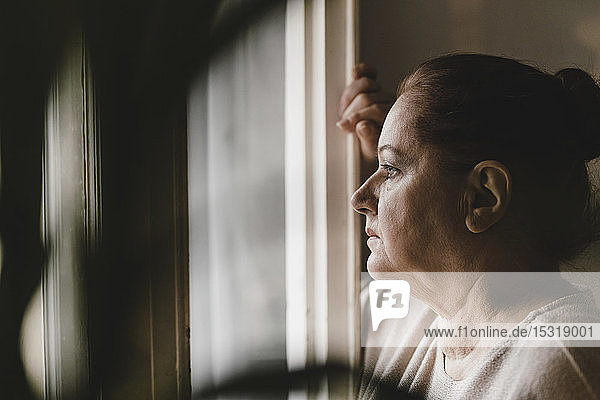 Serious senior woman looking out of window at home