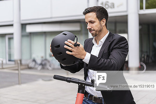 Geschäftsmann mit E-Scooter in der Stadt setzt Helm auf
