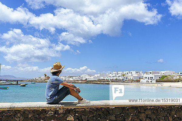 Man sitting on wall looking towards Caleta de Sebo La Graciosa Canary Islands Spain