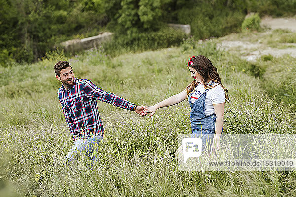 Junges Paar geht über eine Wiese und hält sich an den Händen
