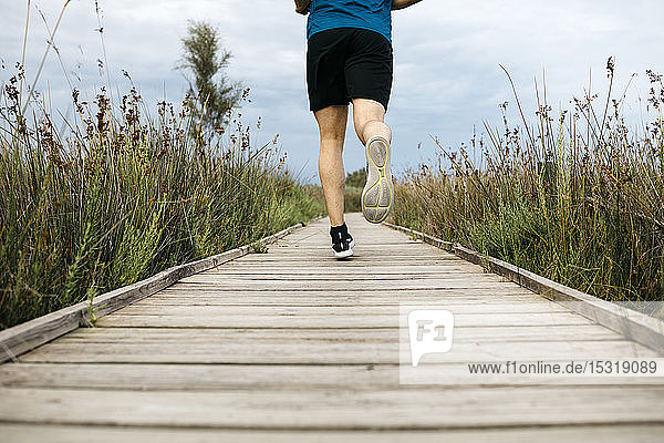 Rear view of a male jogger running on a wooden walkway