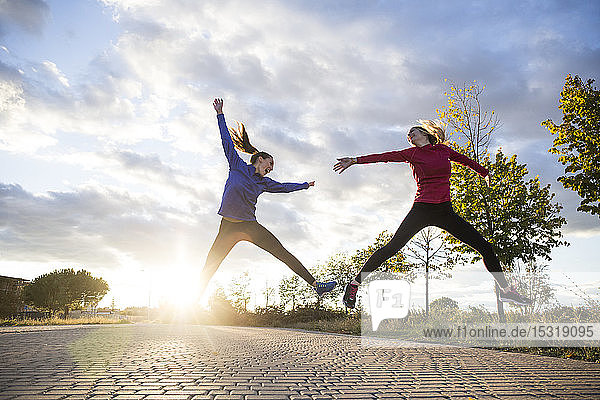 Young women having fun and jumping in park  against morning sun