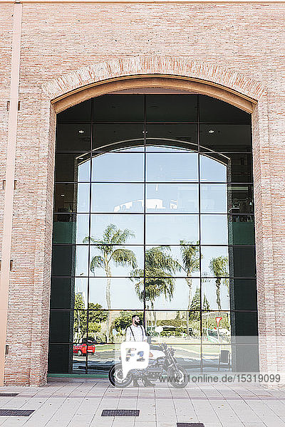 Man standing with motorbike standing in front of glass facade