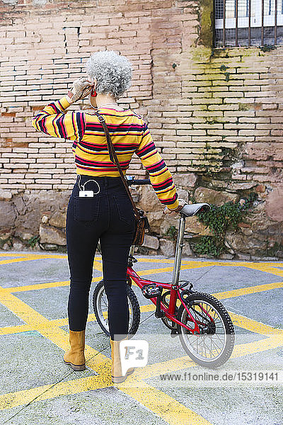 Rückenansicht einer Frau mit Fahrrad  die ein Smartphone in ihrer Tasche trägt