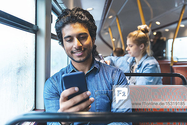 Porträt eines jungen Mannes  der mit dem Bus reist und auf sein Handy schaut  London  UK