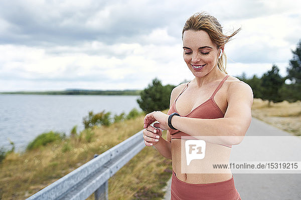 Porträt einer fitten Frau  die beim Joggen im Freien die Smartwatch kontrolliert