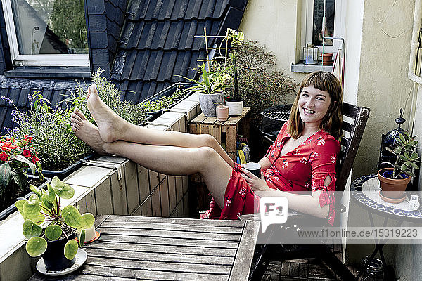 Portrait of smiling young woman relaxing with cup of coffee on balcony