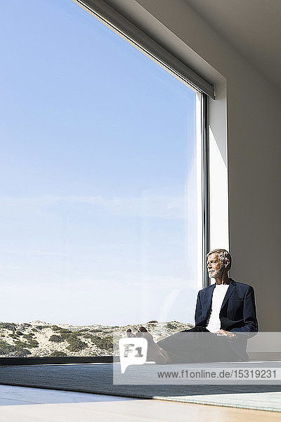 Senior businessman sitting at panorama window looking out